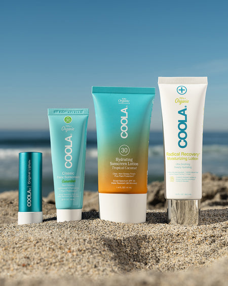 4 travel-sized sunscreen products sitting in sand at beach with scenic ocean view in background