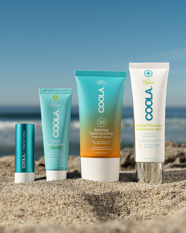 4 travel-sized sunscreen products sitting in sand at beach with scenic ocean view in background