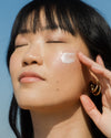 Close-up of woman applying SPF face lotion with blue sky in background