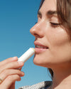 Woman applying SPF lip balm with blue sky in background