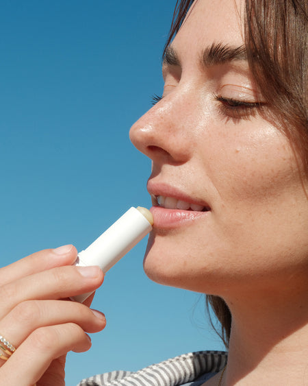 Woman applying SPF lip balm with blue sky in background