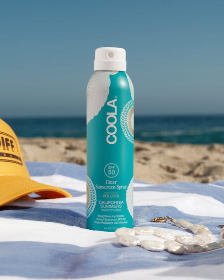 Coola sunscreen spray bottle on a beach with ocean view