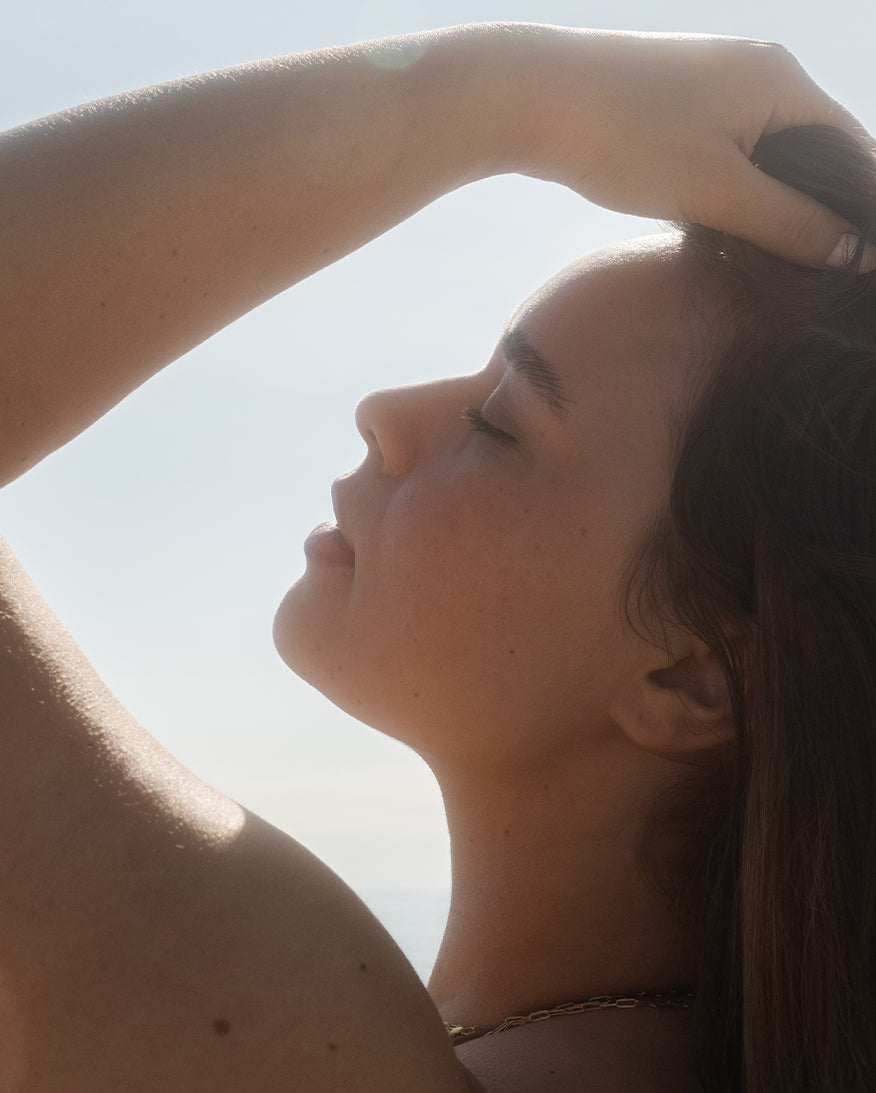 Woman brushing hand through hair, backlit against a sky background.