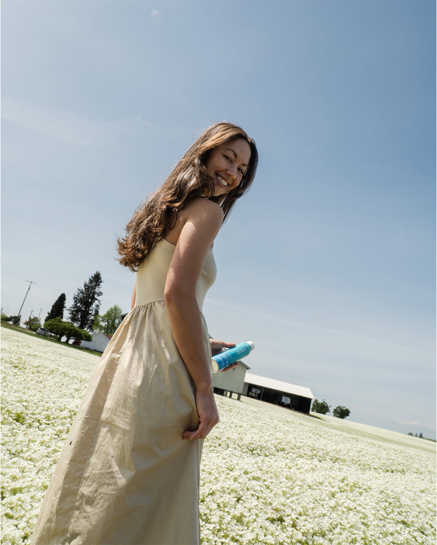 Woman holding blue sunscreen bottle in field of white flowers