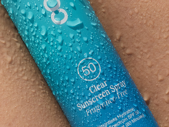 Close-up image of COOLA Clear Sunscreen Spray Fragrance-Free SPF 50 with water droplets on packaging.