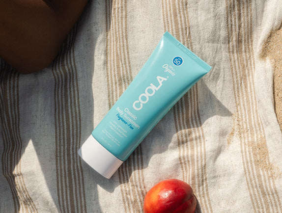 Tube of COOLA Classic Body Sunscreen lotion sitting on a striped beach towel