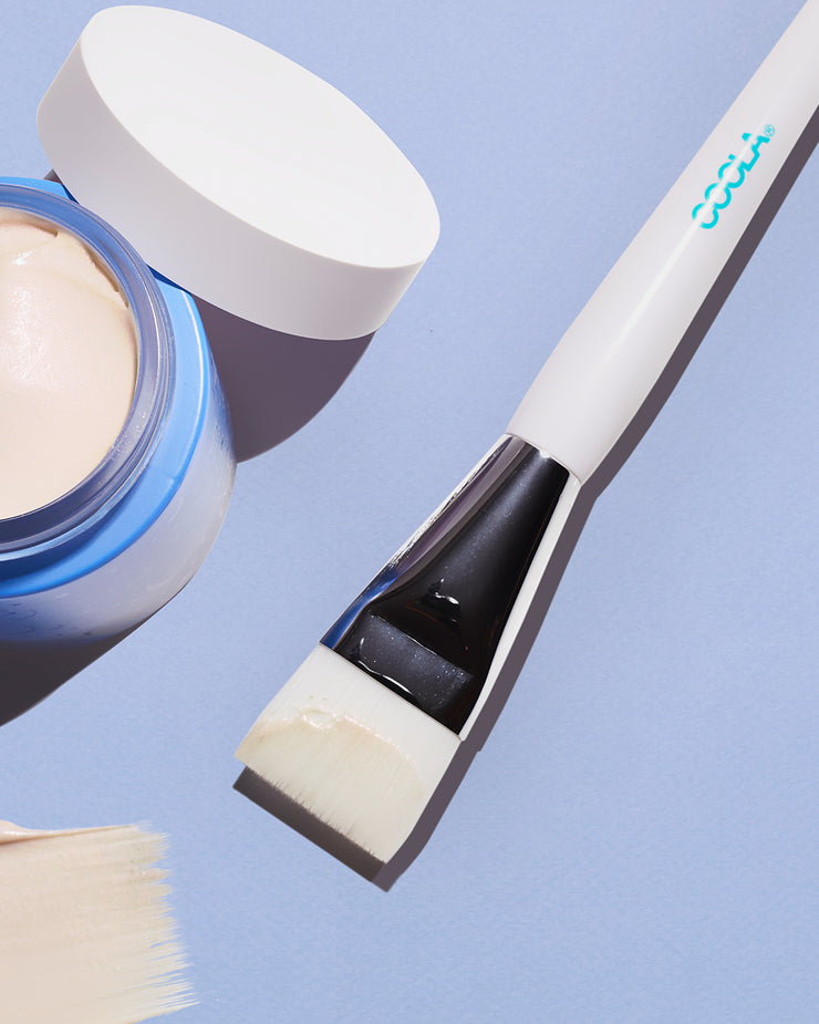 White facial brush and open blue jar sitting on violet surface