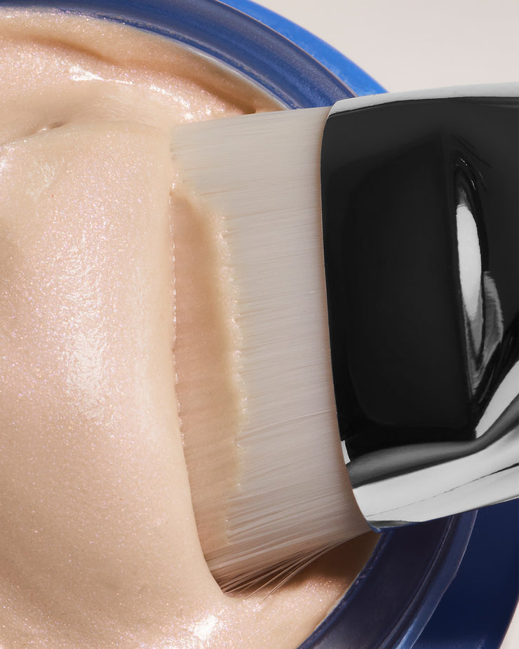 Close-up of white brush dipping into blue jar with a tinted formula