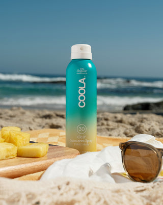 Coola piña colada sunscreen spray bottle on a beach with ocean view