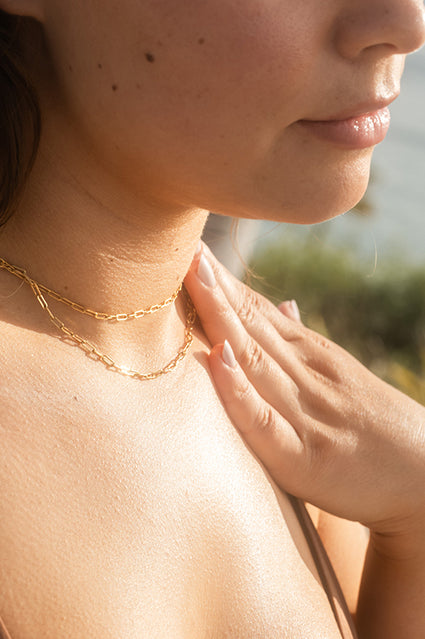 Close-up of woman applying sunscreen lotion to chest with coastal background