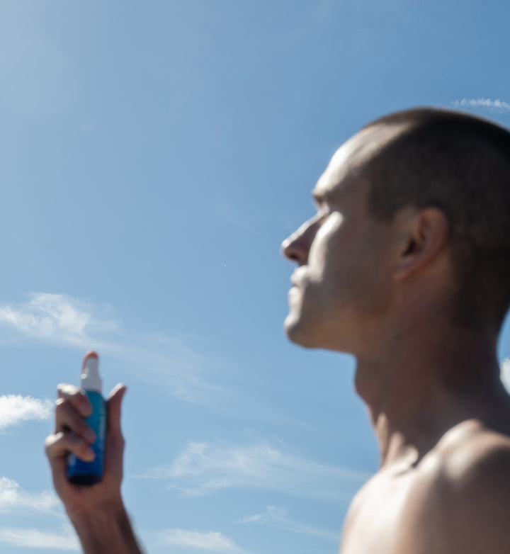 Man applying COOLA Classic Face Mist with blue sky in background.