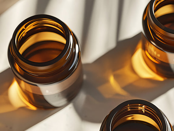 Close up of jars with yellow oil on neutral surface
