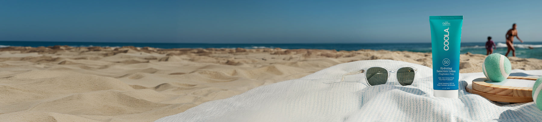 Beach with sunglasses and a bottle of COOLA sunscreen