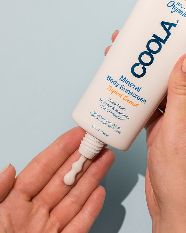 COOLA Mineral Body Sunscreen Lotion Tropical Coconut SPF 30 being dispensed in person's hand with light blue background