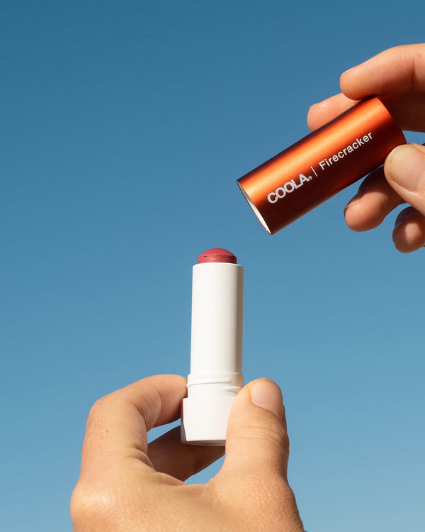 COOLA Firecracker Mineral Liplux with cap taken off showing formula against sky blue background.