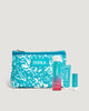 A COOLA suncare travel set with a blue floral print pouch, containing a sunscreen spray, sunscreen face lotion, and lip balm.