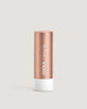A stick of COOLA Liplux Tinted Lip Balm in a rose gold colored tube with the label 'Skinny Dip' on the front.