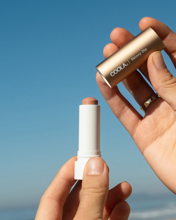 COOLA Skinny Dip Mineral Liplux with cap taken off showing formula against sky blue background.