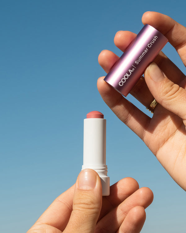COOLA Summer Crush Mineral Liplux with cap taken off showing formula against sky blue background.