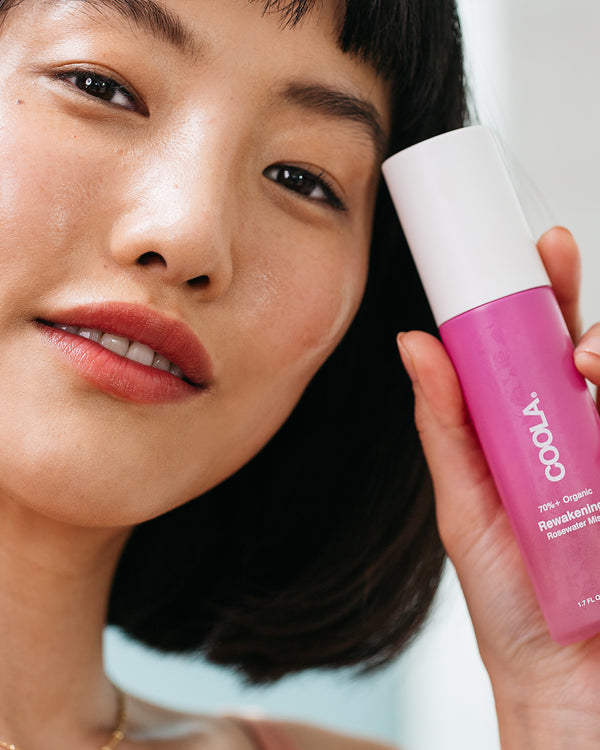 Close-up of woman holding COOLA Rewakening Rosewater Mist with white background.