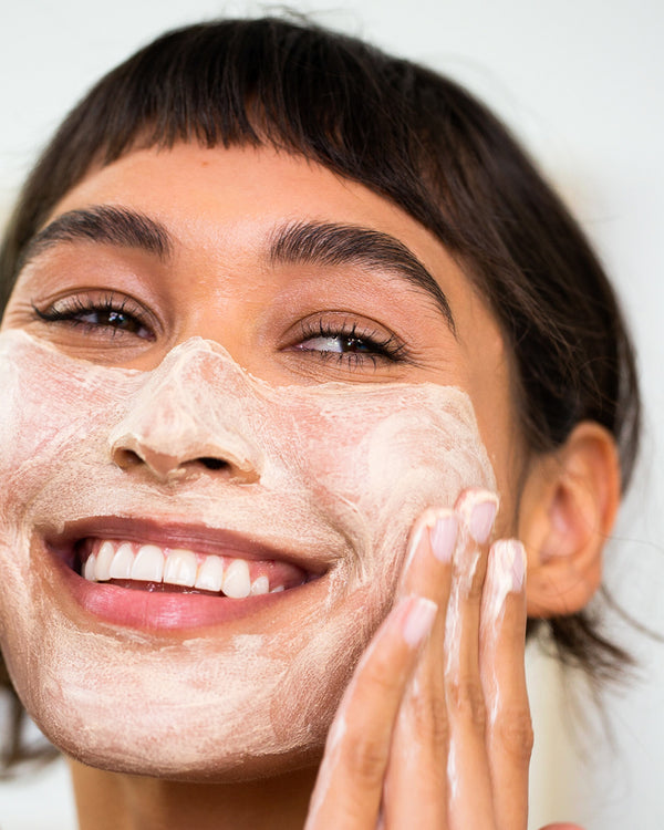 Close-up of woman applying exfoliator to her face with a neutral background