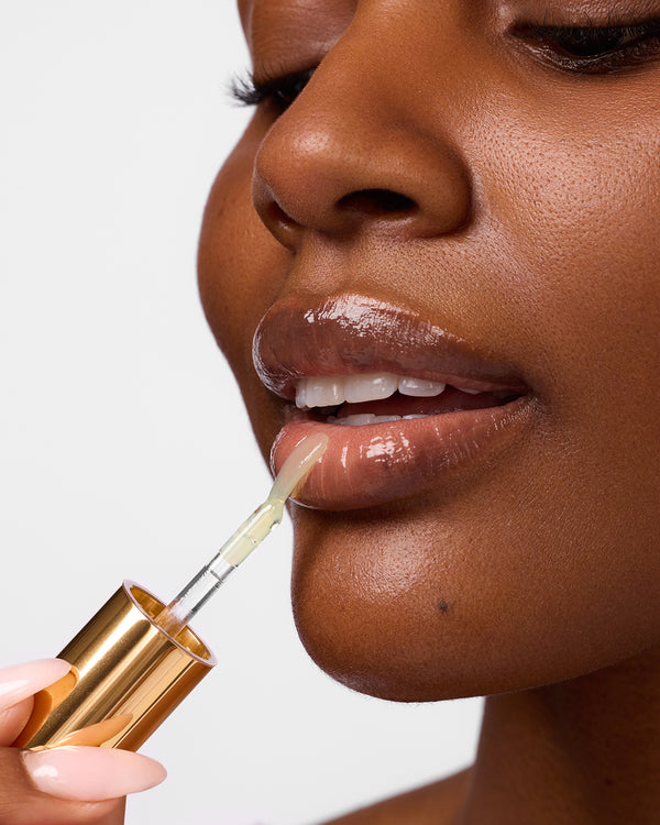 Close-up of woman applying COOLA Liplux Hydrating Lip Oil to lips with white background.
