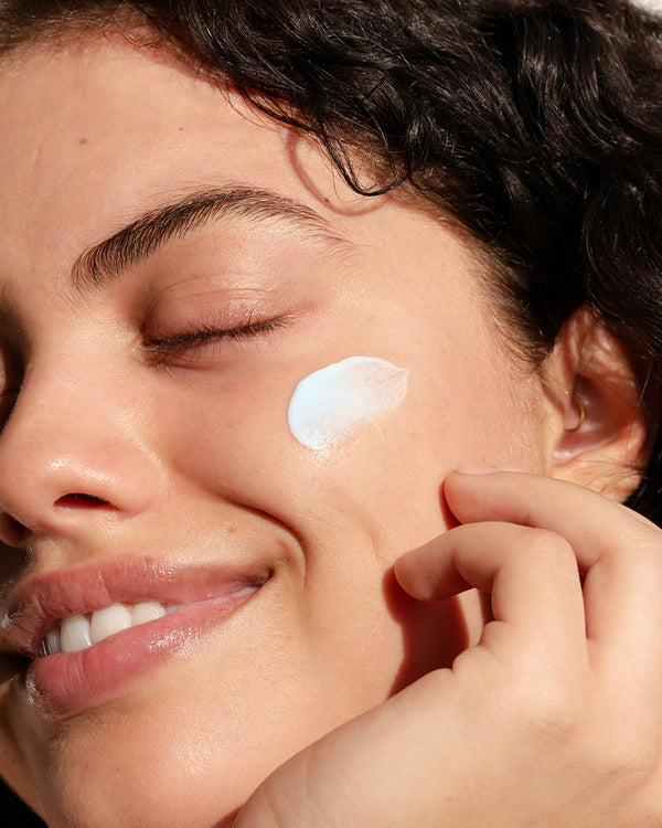 Close-up of woman applying COOLA Refreshing Water Plumping Gel Serum to cheek