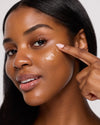 Woman applying cream to her face with a neutral background