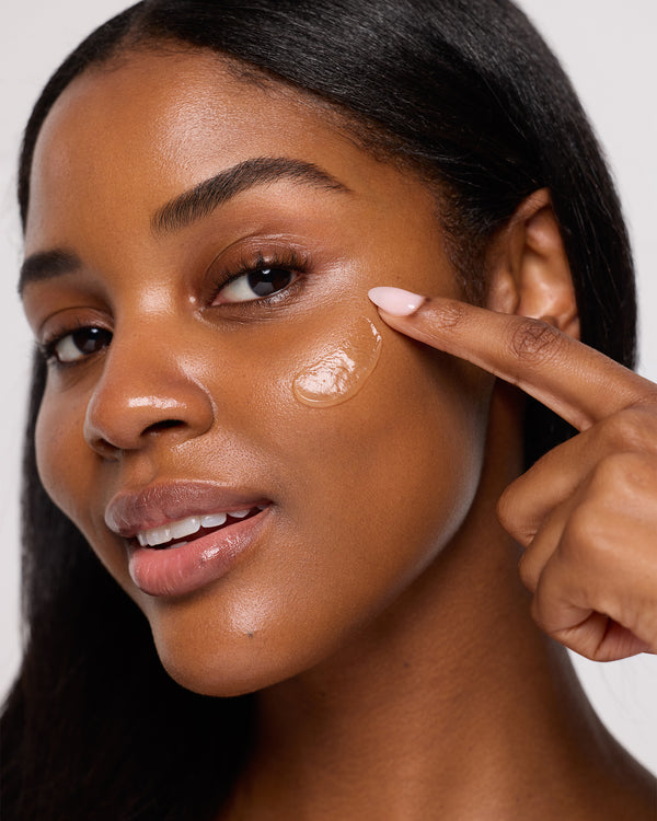 Woman applying cream to her face with a neutral background