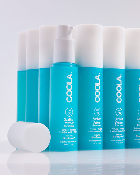 Multiple bottles of Coola sunscreen with white caps on a light gray background