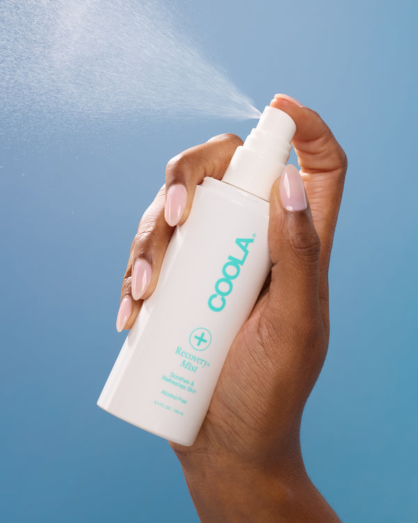 Hand holding a Coola spray bottle against a blue background