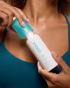 Person using a white bottle with a blue cap on their shoulder, featuring the brand 'Innoa'.