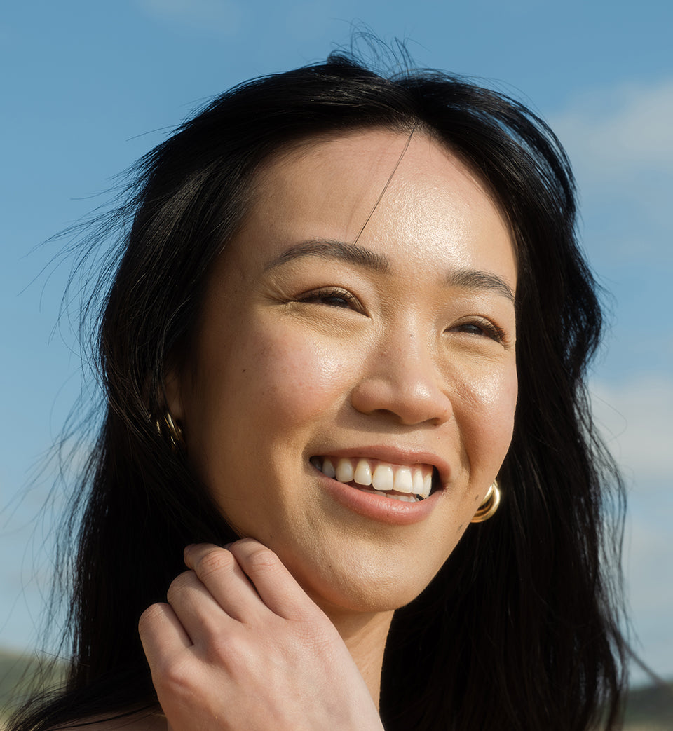 Woman smiling with a moisturized face and blue sky in background.