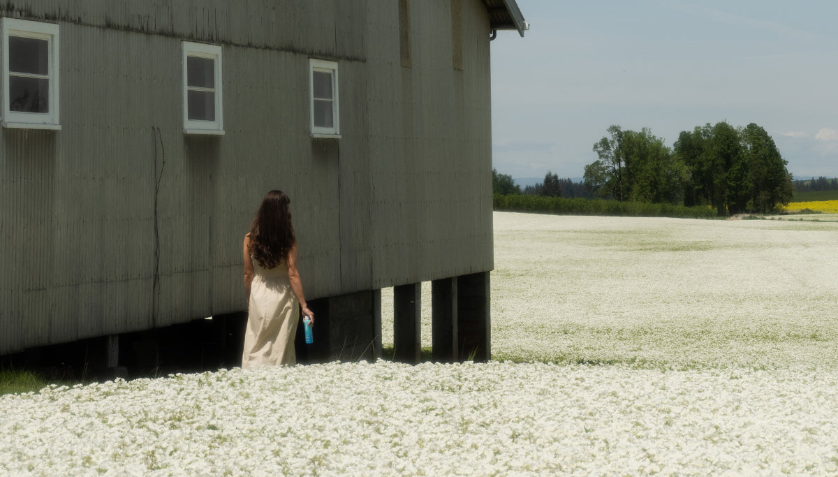 Woman holding sunscreen bottle in field of white flowers