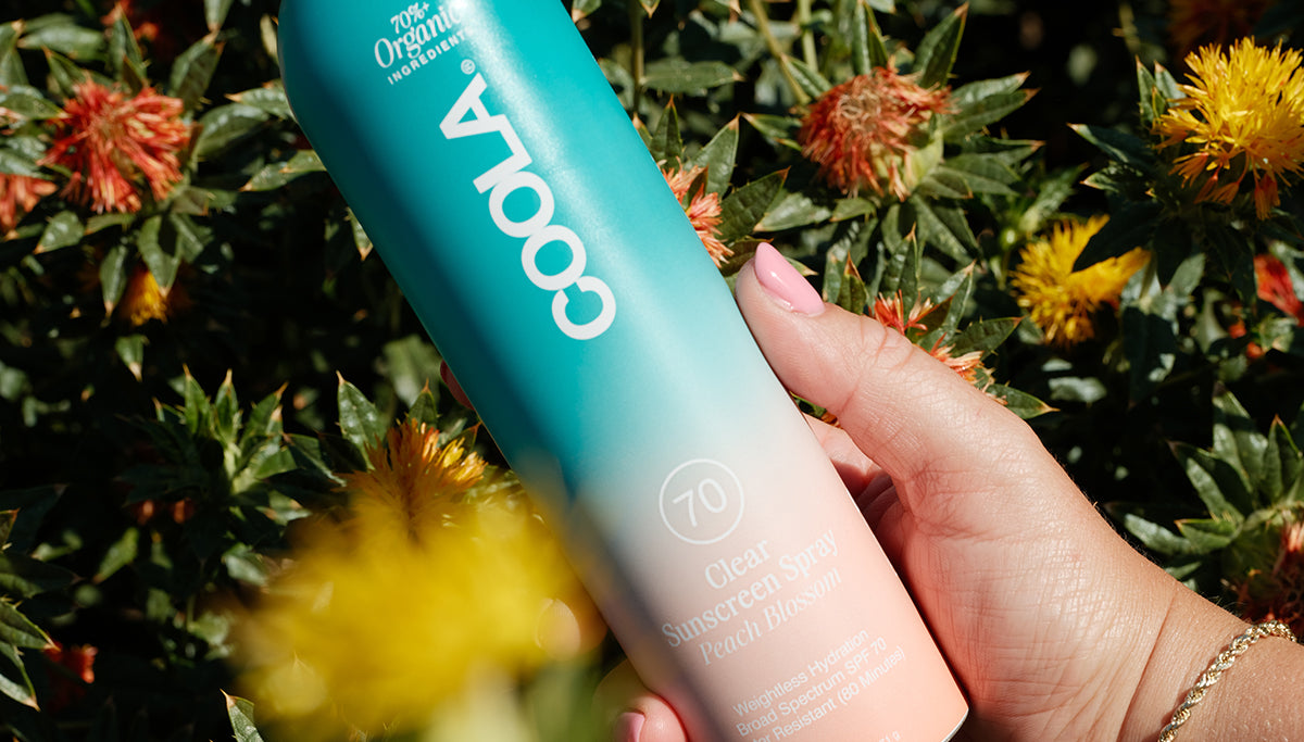 Close-up of COOLA Clear Sunscreen Spray Peach Blossom SPF 70 in field of safflowers