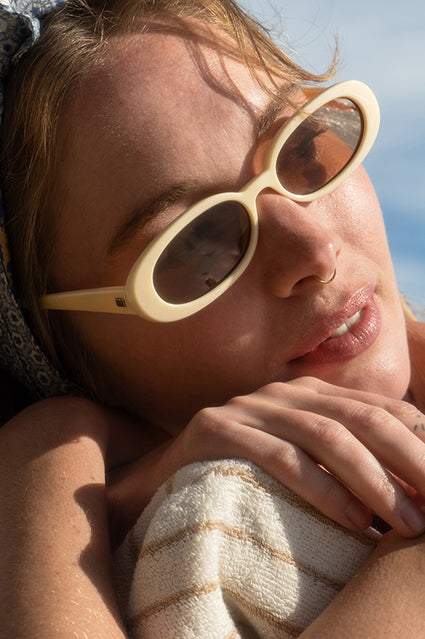 Close=up of woman laying on beach chair with sunglasses on, blue sky in the background.