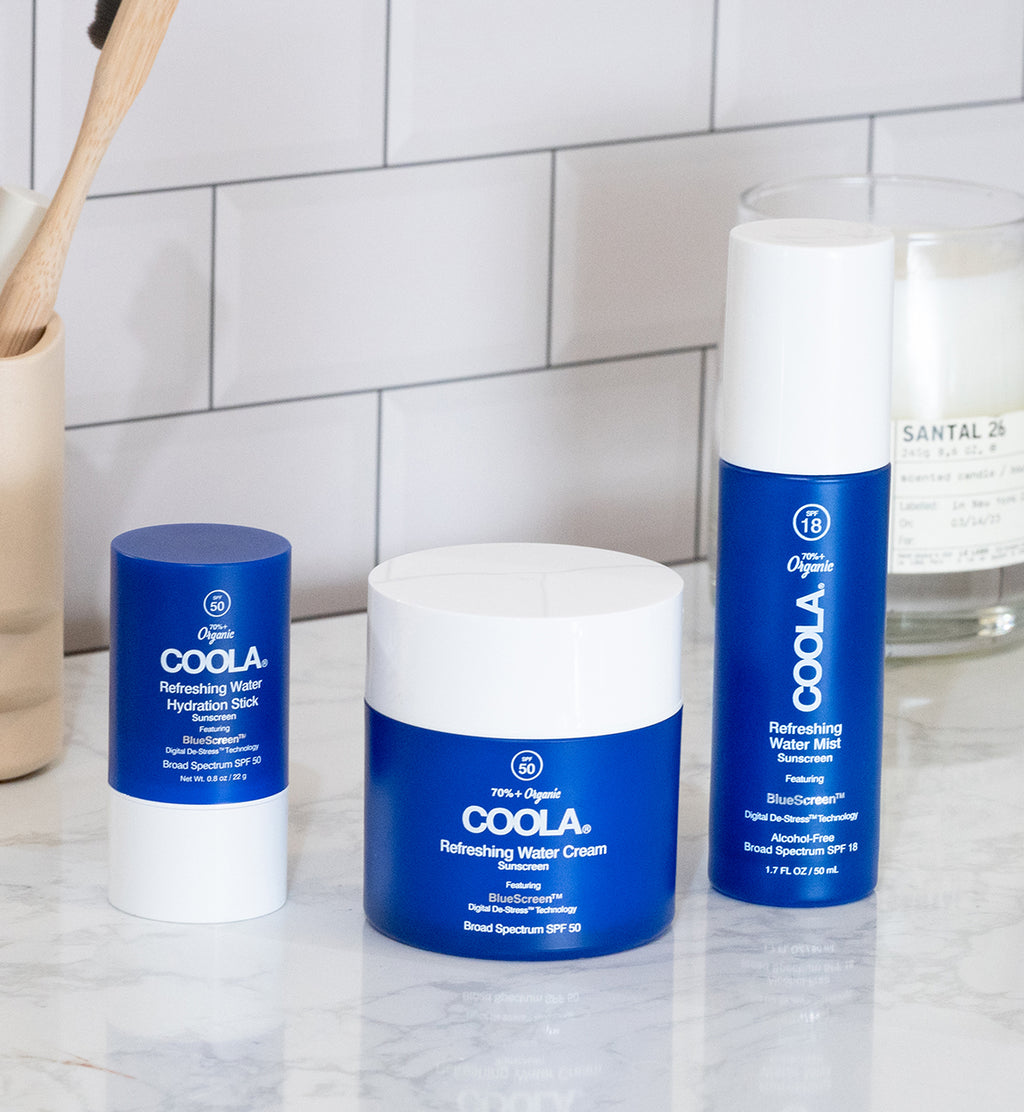 Three blue sunscreen products sitting on bathroom counter with white tiles in background