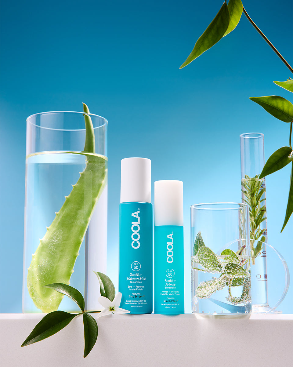Two Coola skincare products with glasses of water and aloe vera leaves on a blue background