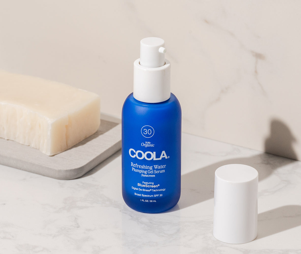COOLA Refreshing Water Plumping Gel Serum SPF 30 bottle on marble surface with cap and soap in background
