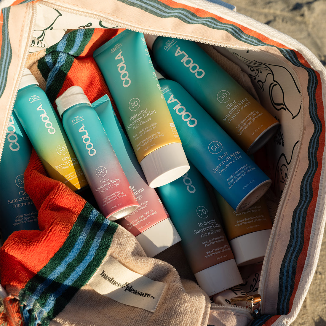 Collection of various sunscreen sprays and lotions inside of a patterned beach bag in the sand at the beach