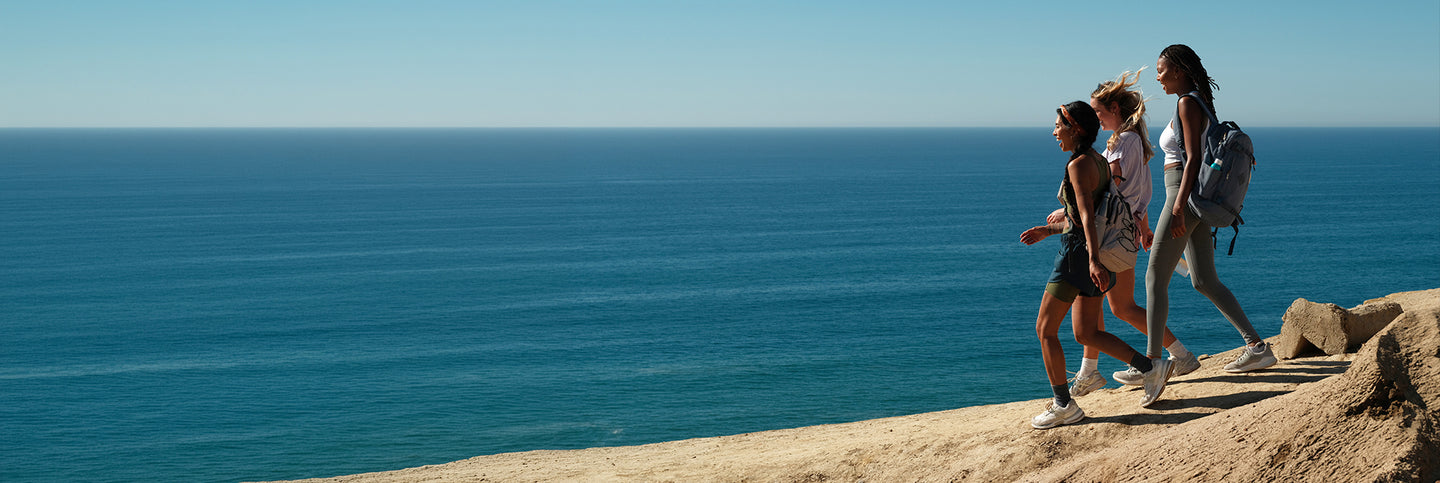 3 Women walking on a cliff next to the blue ocean and sky