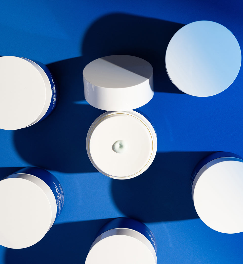 sunscreen jars sitting on blue surface with formula dispensing