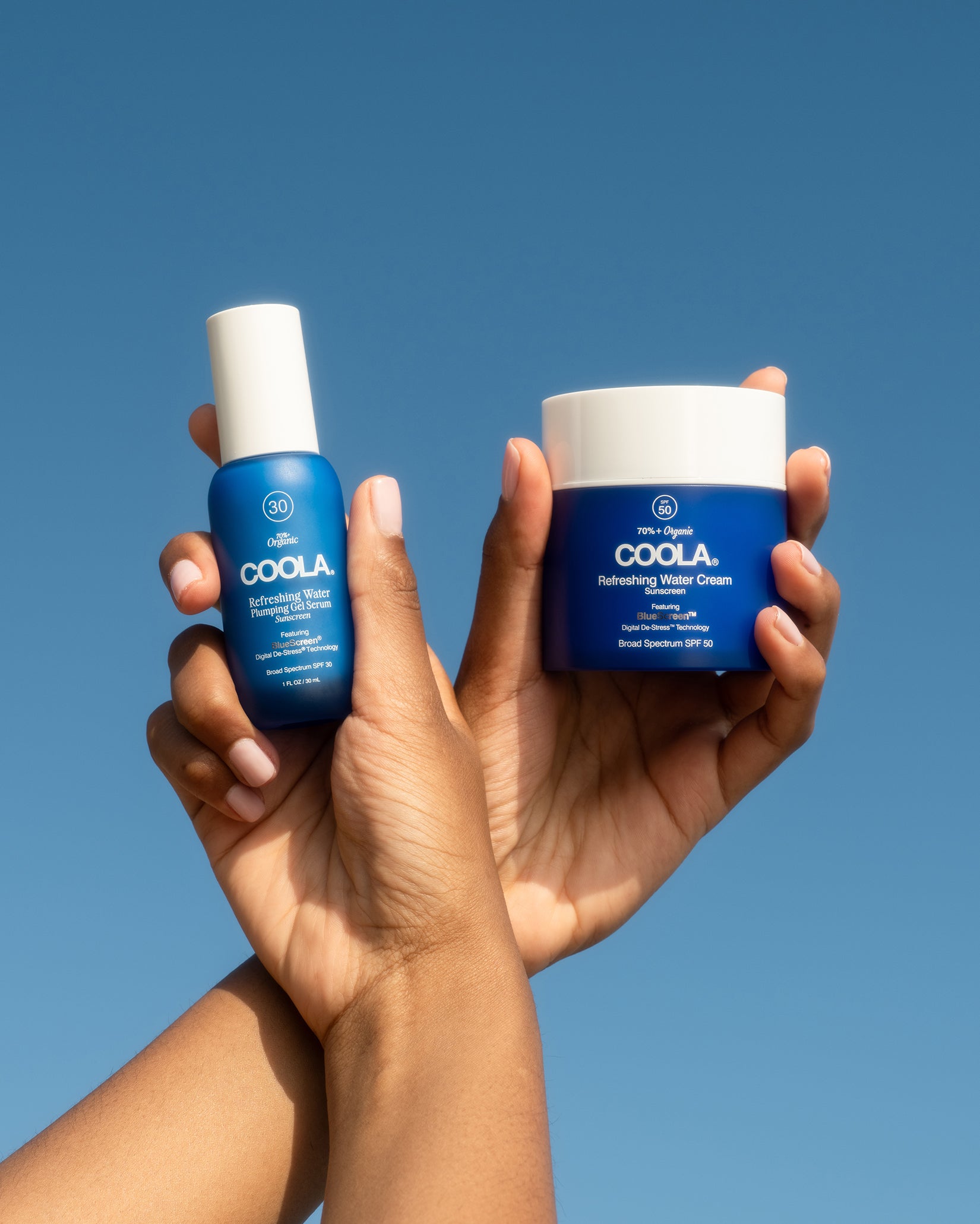 two blue sunscreen products being held towards sky