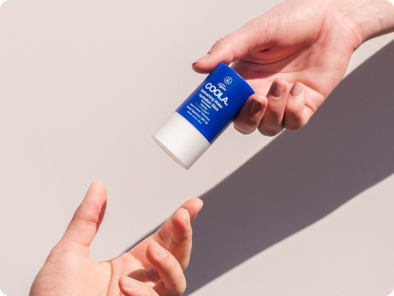 A hand passes a blue and white stick labeled “COOLA” to another open hand, with a neutral light background.
